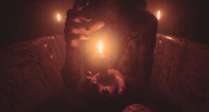 a person with black painted fingernails seen from the neck down holding a lit candle while seated in a bloody bathtub
