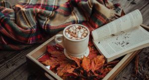 image of a plaid scarf and a tray filled with orange leaves, a mug of hot cocoa, and an open book https://unsplash.com/photos/JhxGkGgd3Sw