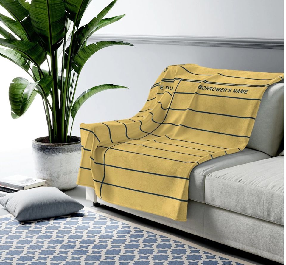 Image of a yellow blanket designed like a library due date card on a gray couch. 