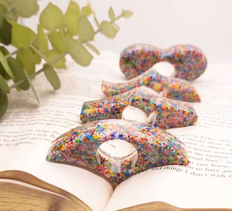Image of several thumb book page holders, each of which looks like it has rainbow sprinkles inside. 