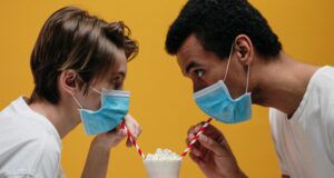 two people drinking a milkshake through straws while still wearing masks around their noses and mouths